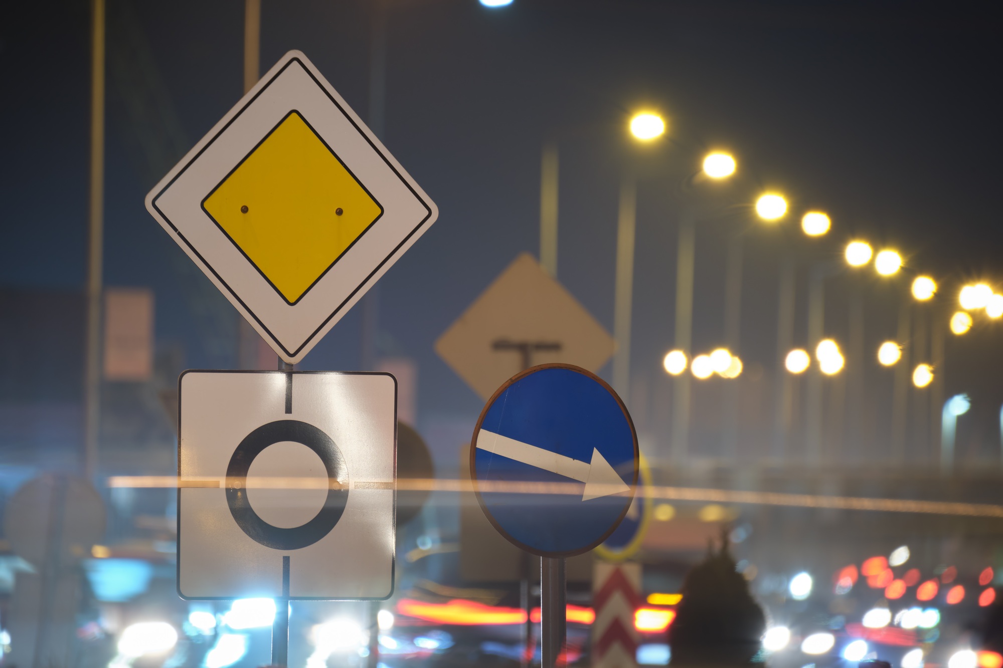 Roundabout road signs with blurred cars on city street traffic at night.